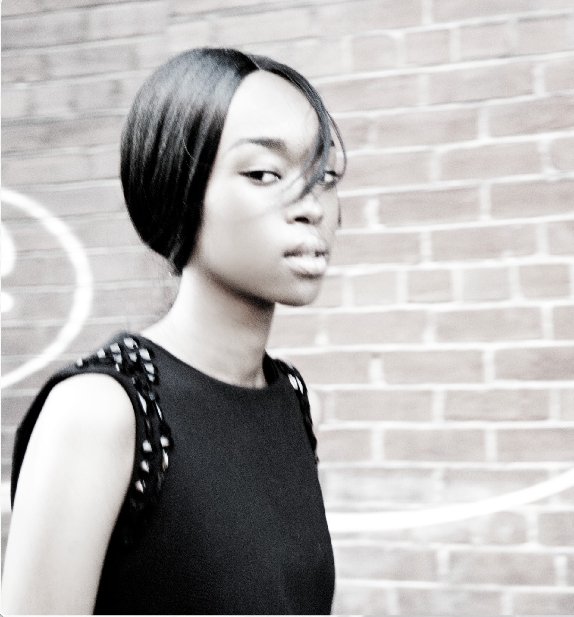 Lamine in a black sleeveless look beside a brick wall