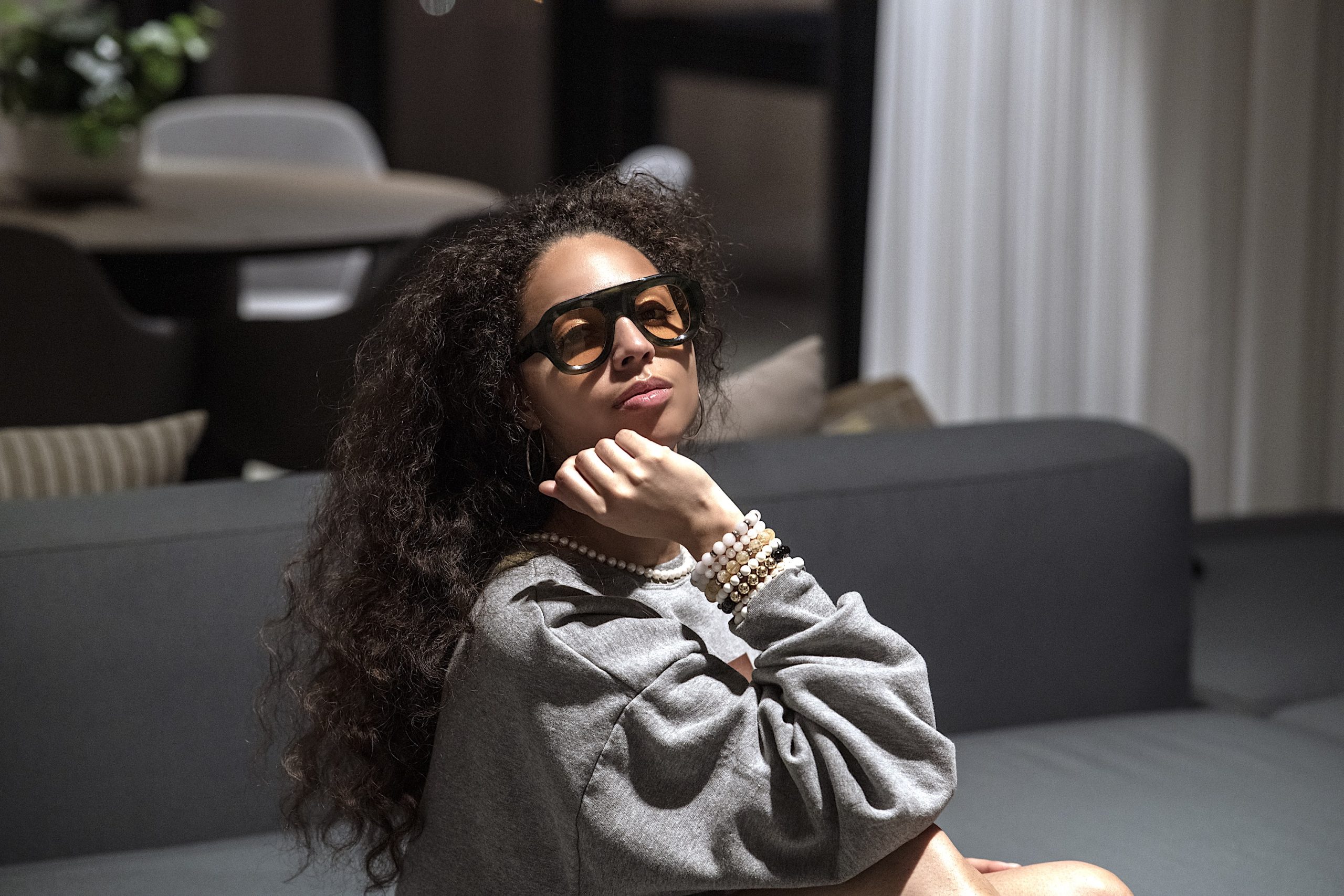 Zelia wearing oversized amber glasses, layered jewellery and an ALLWOOD grey sweatshirt
